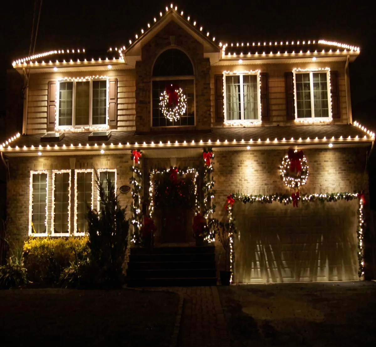 Home outlined in warm white bulbs along the roof, windows and garage, with wreaths on the windows